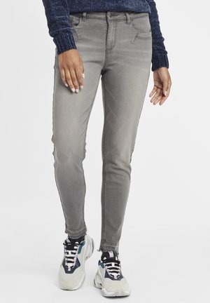 Jeans skinny de denim gris con una textura suave, dos bolsillos frontales y un diseño de tiro medio, combinados con zapatillas gruesas que presentan acentos multicolores.