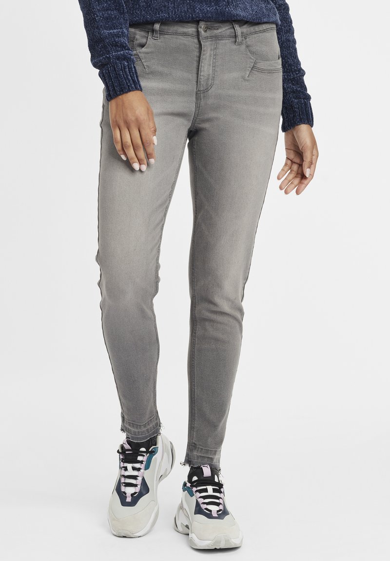 Jeans skinny de denim gris con una textura suave, dos bolsillos frontales y un diseño de tiro medio, combinados con zapatillas gruesas que presentan acentos multicolores.