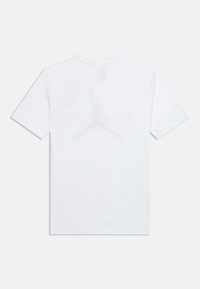 Λευκό κοντομάνικο μπλουζάκι που φαίνεται από την πίσω πλευρά με ένα αχνό, μεγάλο λογότυπο Jumpman και διακριτικό πορτοκαλί κείμενο πίσω από αυτό.