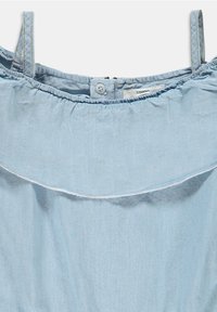Haut en chambray bleu clair avec un col élastique froncé, des straps réglables et un volant décoratif. Fermeture à bouton unique dans le dos.