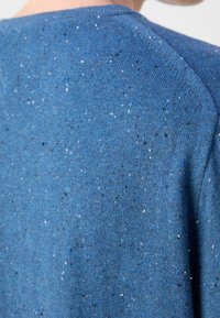 Niebieski sweter z dzianiny o melanżowej fakturze z białymi, czarnymi i niebieskimi włóknami. Okrągły dekolt i wyraźne szwy na ramionach.