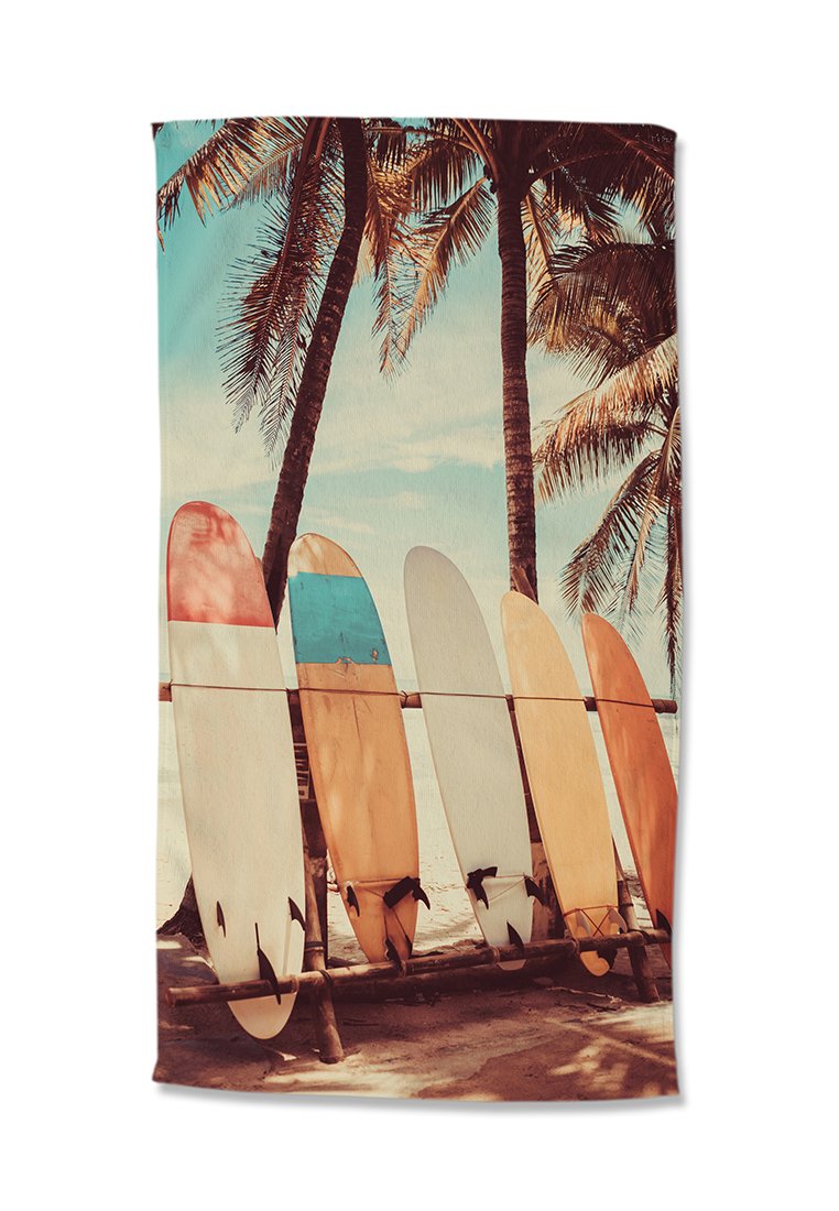 Fünf bunte Surfboards lehnen an einem Holzregal an einem Sandstrand mit Palmen und blauem Himmel im Hintergrund.