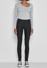 Top gris de manga larga con escote redondeado, combinado con jeans negros ajustados que tienen cremalleras en los tobillos, llevados con zapatillas blancas y negras.