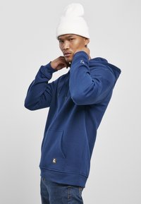 Felpa con cappuccio blu navy realizzata in tessuto morbido, dotata di una tasca frontale e cordini regolabili, con un piccolo logo sulla manica.