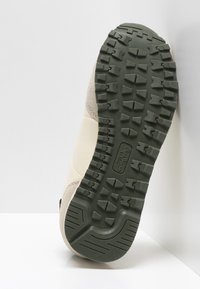 Béžové a šedé tenisky s texturovanou gumovou podrážkou. Podrážka má hluboké drážky pro trakci a mírně zakřivený design paty.