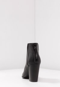 Czarne skórzane botki sięgające kostek z okrągłym noskiem, tylnym zamkiem i masywnym wysokim obcasem. Gładka tekstura i elegancki design.