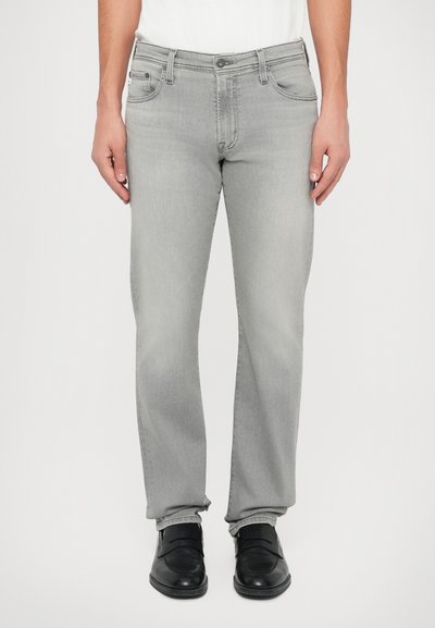 Jean en denim gris clair avec une coupe droite, doté de poches avant, d'une poche à monnaie et d'une fermeture à bouton à la taille. Porté avec des chaussures noires.