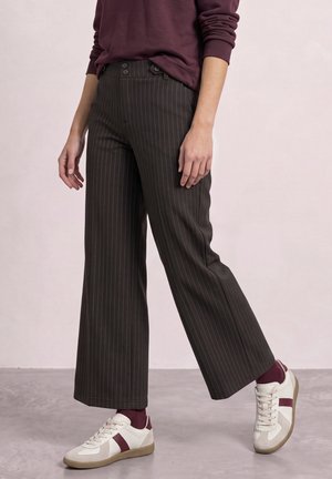 Person iført mørke pinstripe bukser med vide ben, hvide sneakers med bordeaux accenter, bordeaux sokker og en bordeaux langærmet top.