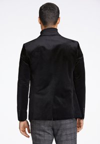 Zwarte fluwelen blazer met een gladde textuur, uitstekend passende snit en enkele knoopsluiting. Heeft slanke revers en knoopmanchetten.