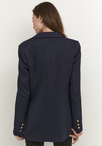 Námořnický blazer s přizpůsobeným střihem, s klopovým límcem, dlouhými rukávy a čtyřmi zlatými knoflíky na každém manžetě. Hladká textura.