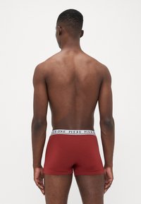 Rote Boxershorts mit einem weißen, markierten Bund, aus glattem Stoff gefertigt. Kurzer Beinschnitt und figurschmeichelndes Design. Minimalistischer Stil.