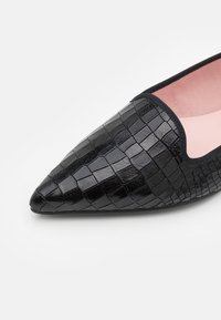 Chaussure plate noire à bout pointu avec une texture brillante effet crocodile et une doublure intérieure rose.