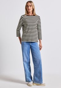 Gestreiftes Langarmoberteil in Schwarz und Creme, kombiniert mit hellblauen weit geschnittenen Jeans. Das Oberteil hat einen runden Ausschnitt und 3/4-Ärmel.