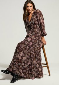 Maximekjole i brun med blomstret paisley mønster. Lavet af letvægtsstof, har lange ærmer, en V-hals og tiered kant.