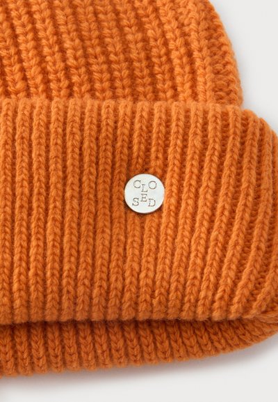 Bonnet en maille côtelée orange avec un revers plié et une petite étiquette métallique ronde argentée gravée du mot "CLOSED".