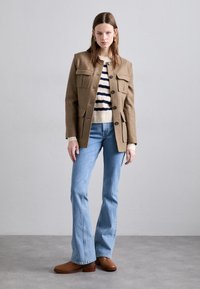 Brown wool jacket with four front pockets, black buttons, paired with a cream and navy striped sweater and light blue flared jeans. Brown heeled boots.