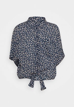 Blouse bleu marine à manches courtes avec petit imprimé floral blanc, boutons devant, poche poitrine et nœud noué à l’ourlet.