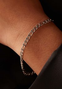 Zilveren kettingarmband om een pols, met elkaar verbonden ovale schakels met een gladde afwerking, tegen een donkere achtergrond.