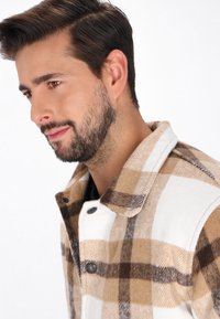 Fleecejacke im braun-weißen Karomuster, ausgestattet mit einem spitzen Kragen und Druckknöpfen, mit einer strukturierten, weichen Oberfläche.