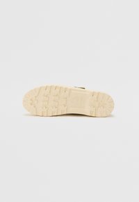 Σόλα παπουτσιού με σκληρό σχέδιο, που διαθέτει βαθιές αυλακώσεις. Το χρώμα είναι κρεμ με υφή, κατάλληλο για διάφορα εδάφη.