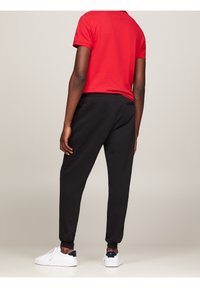 Svarta joggingsbyxor med elastiska muddar, kombinerat med en röd pikétröja. Modellen har på sig vita sneakers med en marinblå detalj på hälen.