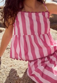 Robe sans manches rayée rose et blanche avec un design à basque et une bordure festonnée, réalisée en tissu léger, offrant une coupe décontractée.