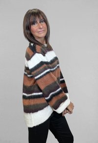 Maglione a righe marroni e bianche realizzato in materiale morbido e peloso, con vestibilità ampia, polsini a costine e orlo stondato più lungo dietro. Indossati pantaloni neri.