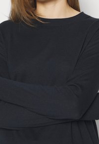 Pull à manches longues bleu marine foncé en tissu tricoté doux, avec un col rond et des détails côtelés subtils aux poignets.