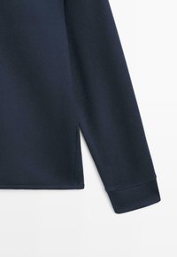 Marineblå langærmet beklædningsgenstand med konisk ærme, sideslidsedetalje, glat tekstur og syede sømme.