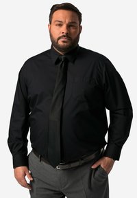 Černá košile s dlouhým rukávem, límečkem a náprsní kapsou, doplněná černou kravatou a šedými kalhotami, s hladkou texturou a přiléhavým střihem.