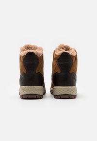 Botas de tobillo de ante marrón y cuero negro con suelas de goma beige, que cuentan con un forro suave y peludo y acentos de tacón estructurado.