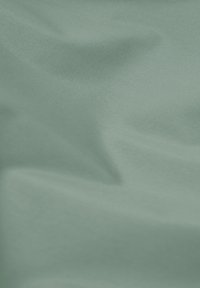 Glattes, hellgrünes Gewebe mit sanften Falten und sichtbarer feiner Struktur, die weiche Schatten und Lichtreflexe erzeugt.