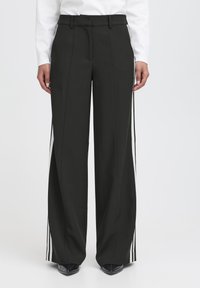 Pantaloni neri a gamba larga con una texture liscia, con strisce laterali bianche e una vita alta. Il tessuto appare leggero e tagliato su misura.