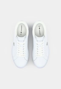 Białe skórzane sneakersy o gładkiej fakturze, zaokrąglonym kształcie noska, wiązane sznurowadłami i z małym zielonym logo po bokach.