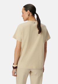 Top beige de manga corta con un escote redondo y una textura suave, que presenta una costura trasera sutil y se combina con pantalones rayados beige.