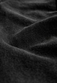 Tessuto nero con una superficie liscia e una leggera lucentezza, caratterizzato da sfumature variabili e pieghe morbide, che suggeriscono un materiale leggero e morbido.