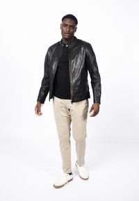 Černá kožená bunda s texturovanými rameny, doplněná černým tričkem, béžovými kalhotami a bílými botami s hnědými podrážkami.