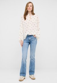 Kremowa bluzka w wzór paisley, z wiązanym dekoltem i bufiastymi rękawami; zestawiona z jasnoniebieskimi dzwonami i beżowymi trampkami.