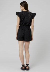 Combinaison en tissu à œillets noirs avec des manches courtes à volants, taille élastique et short assorti. Caractéristiques de motifs découpés complexes.