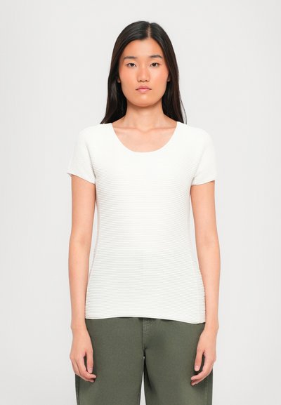 Haut à manches courtes blanc avec un col rond, en tissu côtelé texturé et à la coupe ajustée. Associé à un pantalon vert olive.