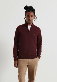 Felpa zip-up bordeaux in tessuto a coste, con un piccolo logo sul petto, abbinata a pantaloni beige. Design semplice e aderente.