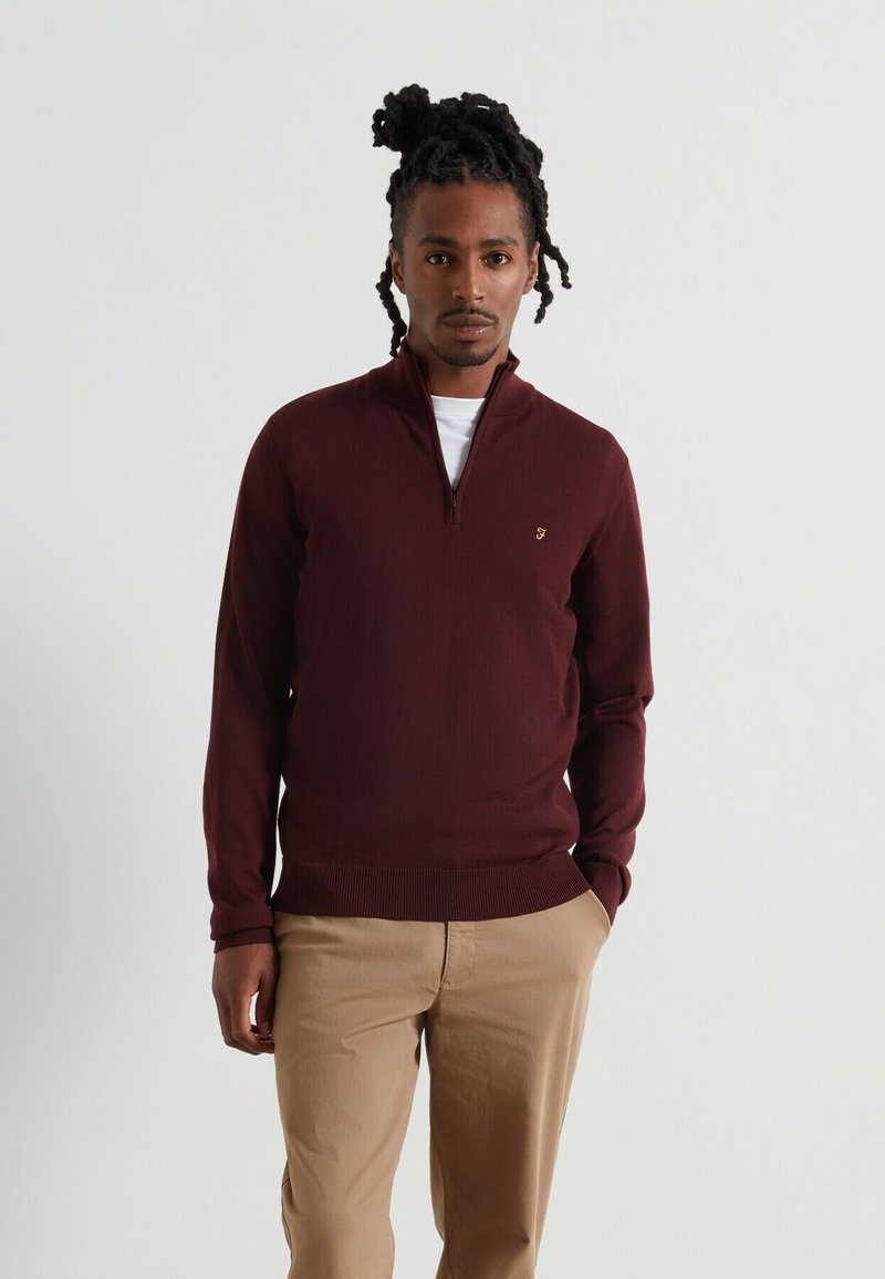 Felpa zip-up bordeaux in tessuto a coste, con un piccolo logo sul petto, abbinata a pantaloni beige. Design semplice e aderente.