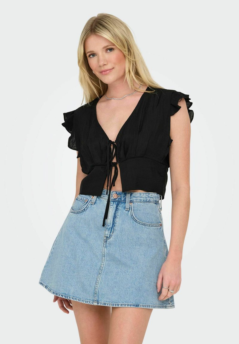 Schwarze, kurvennahe Bluse mit Rüschensäumen und einer Schlaufe zum Binden an der Vorderseite, kombiniert mit einem hochgeschnittenen, hellblauen Jeansrock. Schlichtes Design.