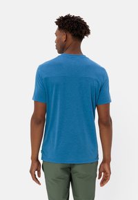 Blauwe t-shirt met korte mouwen en ronde hals, met een subtiele textuur en een rechte zoom. Draagt bij groene broek.