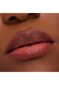 Zbliżenie na pełne usta pomalowane matową, nude różową pomadką, ukazujące subtelną teksturę i naturalne wykończenie na tle ciepłych tonów skóry.