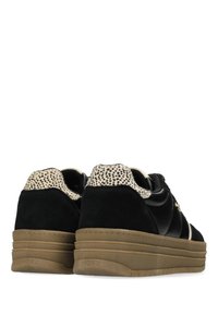 Baskets en daim noir avec une semelle texturée beige, dotées d'un col beige tacheté et d'un accent logo doré sur le côté.