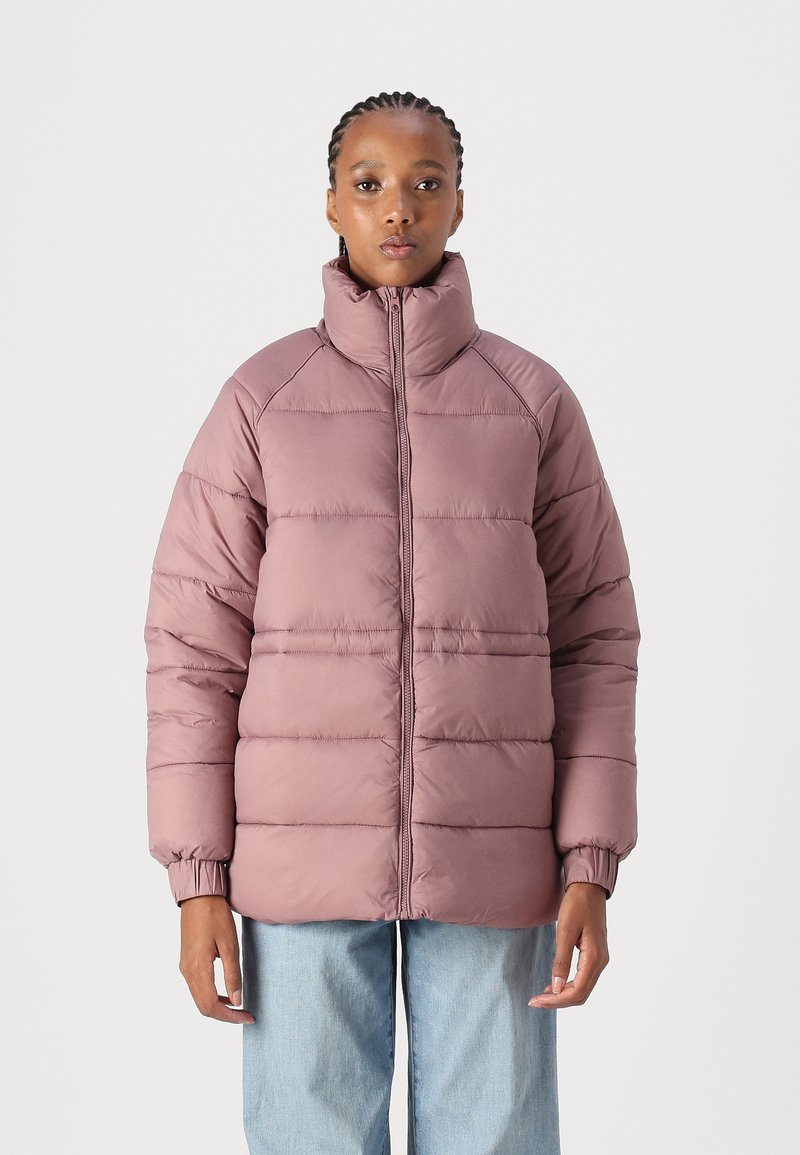 Pastellrosa polstret jakke med høy krage, lange ermer, ribbestrikkede mansjetter og horisontale sømdetaljer. Kombinert med lyseblå denimbukser.