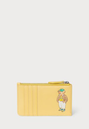 Cartera de cuero amarilla con cierre de cremallera, múltiples compartimentos para tarjetas y un personaje de oso impreso con chaqueta y gorra. Textura suave.