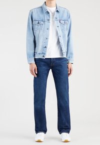 Ljusblå jeansjacka med knappstängning, i kombination med en vit t-shirt, mörkblå jeans och vita sneakers med gummisulor.