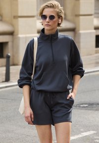 Dark gray pullover with a high neckline and half-zip, paired with matching shorts. Features a front pocket and relaxed fit.